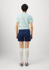 Ljusblå skjorta med geometriskt mönster och korta ärmar, marinblå shorts, vita knästrumpor och svarta fotbollsskor med röda detaljer.