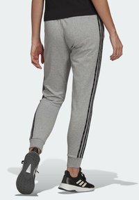 Grå joggers med svarta sidostrips, åtsittande ärmslut och en slät textur, kombinerat med svarta träningsskor med vita accenter.