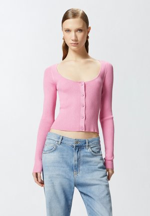 Cardigan de manga larga de color rosa con textura acanalada, escote redondeado y botones en la parte frontal, combinado con jeans de mezclilla azul claro.
