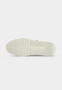 Semelle d’une chaussure blanche avec des rainures horizontales et verticales pour la traction, montrée sur un fond clair uni.