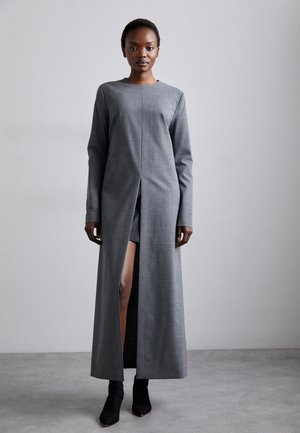 Graues langärmliges Kleid mit einem hohen Schlitz bis zum Oberschenkel, aus strukturiertem Stoff. Hat einen Rundhalsausschnitt und einen geraden Schnitt. Getragen mit schwarzen Knöchelstiefeln.