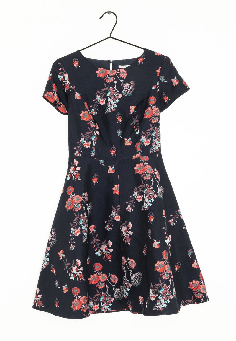 Robe florale sur un cintre, avec un fond bleu marine, des manches courtes et des fleurs multicolores en rouge, rose et bleu. Jupe évasée.