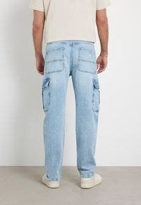 Pantaloni cargo in denim azzurro chiaro con una vestibilità morbida, doppie tasche laterali e due tasche posteriori con un dettaglio logo. Le calzature sono bianche.