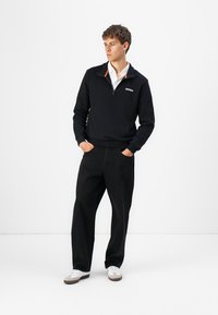 Black fleece pullover with quarter-zip and orange accent, paired with loose-fitting black pants and white sneakers. Simple design, casual style.