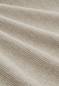 Tessuto di color crema con un sottile motivo a spina di pesce. Il tessuto ha una texture morbida e presenta pieghe leggere per un aspetto stratificato.