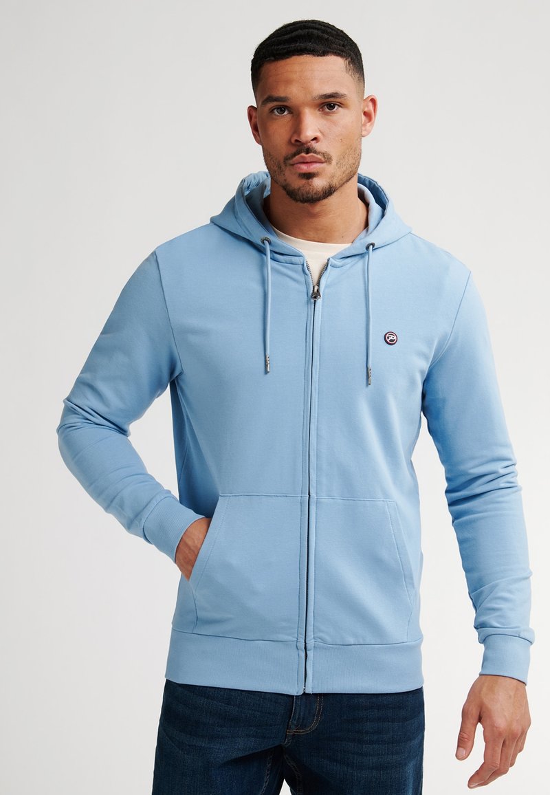 Hellblaue Reißverschluss-Hoodie aus weichem Material mit einer vorderen Tasche, Kordeln für die Kapuze und einem kleinen Logo auf der Brust.