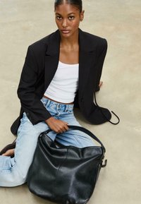 Schwarze Leder-Hobo-Tasche mit geschwungener Form und weicher Textur, ausgestattet mit einem Einzelgriff und minimalen Nähten, neben hellblauen Jeans platziert.