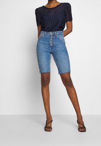Shorts en jean taille haute, lavage clair, ourlet effiloché, fermeture à cinq boutons, associés à un haut en maille à manches courtes bleu marine avec un motif texturé.