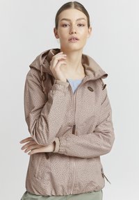 Giacca leggera di colore rosa pallido con piccoli motivi a pois, cappuccio regolabile, polsini elasticizzati e tasche laterali con chiusura a zip.