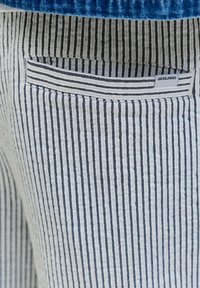 Nahaufnahme einer schwarz-weiß vertikal gestreiften Stofftasche mit einem kleinen weißen Etikett mit der Aufschrift „JACK & JONES“, das am Rand angenäht ist.