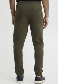 Olivgrüne Jogginghosen mit elastischem Taillenbund und Bündchen an den Knöcheln. Verfügt über eine Gesäßtasche und einen glatten, leicht strukturierten Stoff.