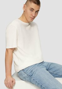 Weißes Kurzarm-T-Shirt mit lockerer Passform, glatter Textur und Rundhalsausschnitt, kombiniert mit hellblauen Denim-Jeans.