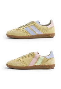 Baskets en daim beige à profil bas avec semelles en gomme, affichant des rayures pastel bleues, roses et vertes sur les côtés et une fermeture à lacets.