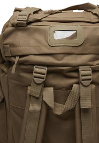 Sac à dos tactique beige montrant des bretelles rembourrées, des boucles, une tirette de fermeture éclair et une fenêtre d'identification transparente sur le rabat supérieur.