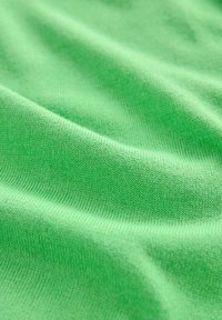 Groene katoenen stof met een gladde textuur, die fijne weefpatronen en zachte plooien toont, waardoor een zachte, vloeiende uitstraling ontstaat.