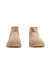 Botines beige de ante con textura suave, punta redonda y suela plana de goma. Presentan costuras laterales y un detalle sutil de pespuntes.