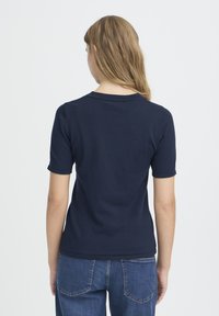 T-shirt en maille bleu marine à manches courtes, col rond et texture lisse, assorti à un jean en denim bleu avec poches arrière.