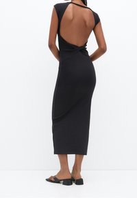Robe noire ajustée avec un dos à découpe profonde, des manches courtes et un détail torsadé à la taille. Le matériau semble lisse et extensible.