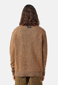 Cardigan marrone con texture, dal fit largo, con bordi a coste e un'etichetta sul collo. Presenta un motivo a macchie distintivo su tutta la superficie.