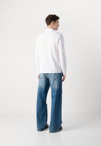 Langermet hvit skjorte kombinert med vide lyseblå jeans. Jeansene har en falmet tekstur og baklommer, iført svarte sko.