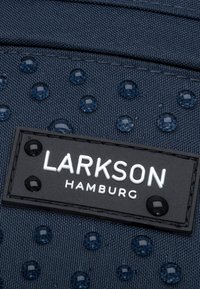 Tessuto struttura blu navy con punti trasparenti in rilievo e un'etichetta nera rettangolare che mostra "LARKSON HAMBURG" in caratteri bianchi.