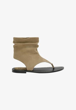 Sandalo alla caviglia in suede color dorato con superiore arrotolato, punta aperta e sottopiede sottile nero. Presenta un design a infradito e dettagli minimi.