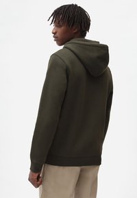 Sudadera con capucha verde oscuro que presenta un corte relajado, textura suave y puños acanalados. La parte posterior muestra un diseño simple y limpio.