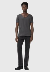 T-shirt grigia a maniche corte con scollatura ampia, abbinata a jeans neri a gamba dritta e calzature nere. Design semplice e casual.