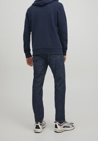 Navy mikina s jemnou texturou, spárovaná s tmavě modrými džíny. Boty mají černé a bílé detaily, s červenými a šedými akcenty.