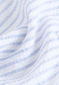 Tissu en coton avec un motif à rayures blanches et bleu clair, comprenant des rayures alternées texturées et lisses, créant une surface douce et respirante.