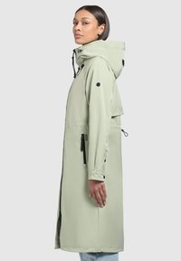 Long, light green waterproof coat with a hood, black accents, and zippered pockets. Features a straight cut and buttoned cuffs.