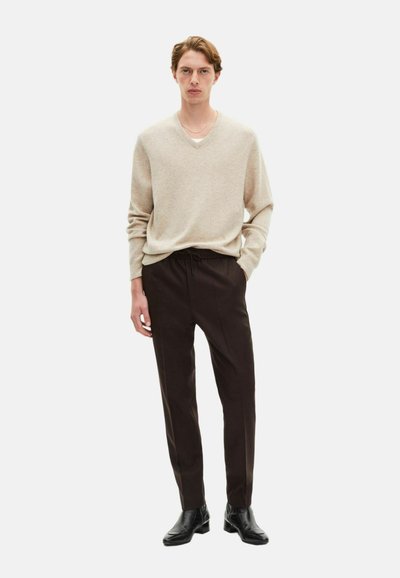 Beige v-hals trui gemaakt van zachte stof, gecombineerd met losse donkere broeken en zwarte enkelboots, wat zorgt voor een gestroomlijnd silhouet.