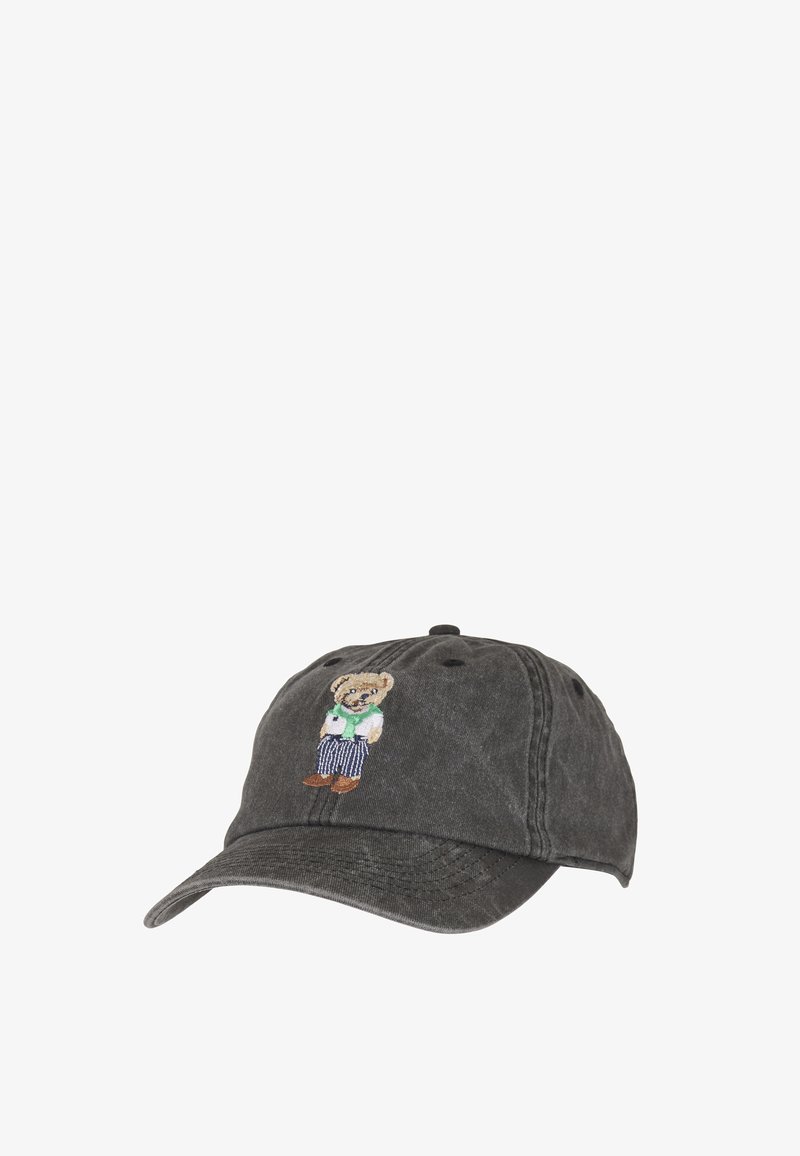 Casquette de baseball noire avec un ours brodé portant un pull vert, une chemise blanche, un pantalon rayé et des chaussures marron au centre devant.