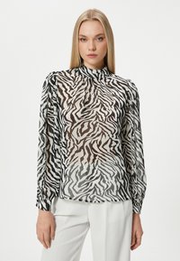 Durchsichtige Bluse mit schwarz-weißem Zebra-Print, langen Ärmeln, hohem Kragen und gerafften Manschetten, konzipiert mit einem leicht lockeren Schnitt.