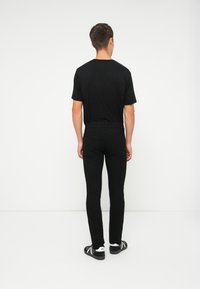 Un tricou negru din bumbac, asortat cu blugi negri skinny. Caracteristicile notabile includ un design simplu și un stil minimalist. Încălțămintea este neagră și albă.