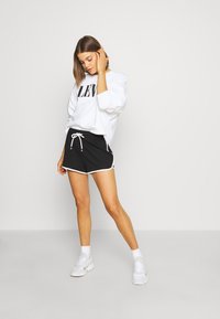 Sweatshirt branco com o texto "LEVI'S", combinado com calções desportivos pretos com cordão e detalhes brancos, complementados por ténis brancos.