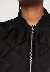 Zwarte gewatteerde bomberjack met ritssluiting met ronde trekker, geribde kraag en gladde textuur.