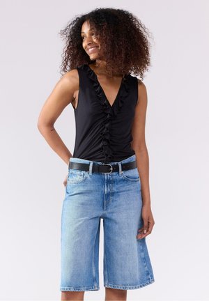 Svart ärmlös topp med en volang framtill, kombinerad med ljusblå denim Bermuda-shorts och ett svart bälte med silverdetaljer.