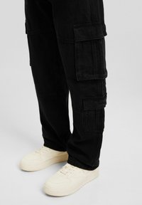 Czarne spodnie typu cargo wykonane z bawełny, z licznymi kieszeniami i luźnym krojem, zestawione z białymi tenisówkami.