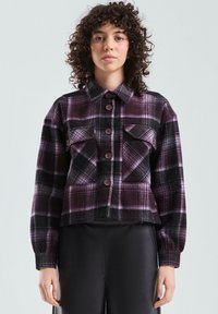 Fioletowo-czarna flanelowa kurtka w kratę z zapięciem na guziki, dwoma kieszeniami na piersi i długimi rękawami. Materiał o fakturze, krótki dół.