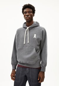 Grijze hoodie gemaakt van zachte stof met een voorkant zak, verstelbare witte trekkoorden en een klein logo op de borst. Beschikt over raglan mouwen.