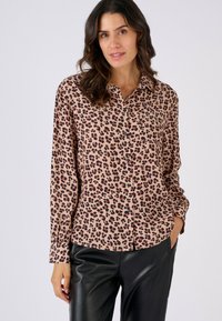 Leopard print blouse in lightweight fabric, featuring long sleeves, a collar, and buttons. The base color is beige with black and rust spots.