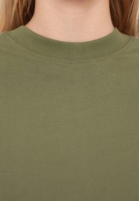 Χακί πράσινο βαμβακερό t-shirt με ριμπ λαιμόκοψη και λεία υφή. Το ύφασμα φαίνεται απαλό και εφαρμοστό, χωρίς εμφανή μοτίβα.