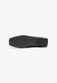 Chaussure à talon haut noire avec une tige en cuir lisse, une pointe effilée et une semelle en caoutchouc texturé dotée de rainures horizontales pour une meilleure adhérence.
