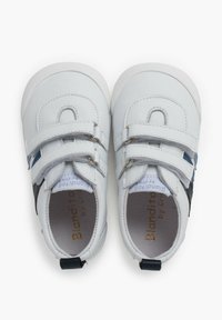 Scarpe in pelle bianca con due cinghie in Velcro, punta arrotondata e un dettaglio laterale blu. Fodera interna morbida e un accento nero nel tallone.