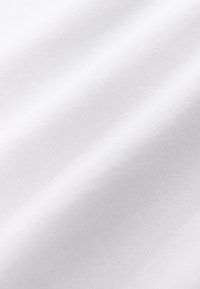 Nahaufnahme einer weißen gewebten Stoffstruktur mit dezenten diagonalen Falten und weichem Licht.