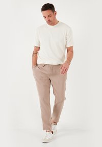 Beige bukser og en ribbet hvid t-shirt, parret med hvide sneakers. Outfittet har en afslappet pasform og blød stofstruktur.