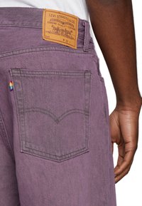 Lila Jeans aus Denim mit einem braunen Lederpatch, auf dem das Logo "Levi Strauss & Co." zu sehen ist; die Gesäßtasche hat ein Regenbogenetikett und eine markante Steppnaht.