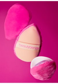 Beautyblender-sponsen in zachte roze en beige tinten hebben een gladde, afgeronde vorm. Eén spons heeft een gestructureerd, zacht oppervlak, terwijl de andere glad is.