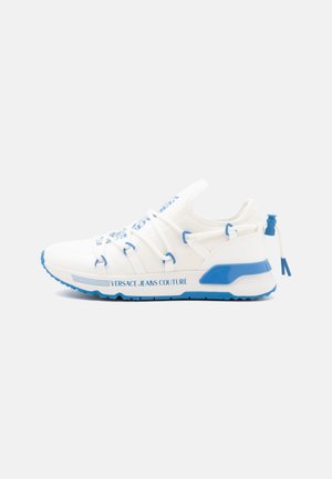 Hvid og blå Versace Jeans Couture sneaker med blå accenter, elastiske snørebånd og brandet sål på en lys grå baggrund.